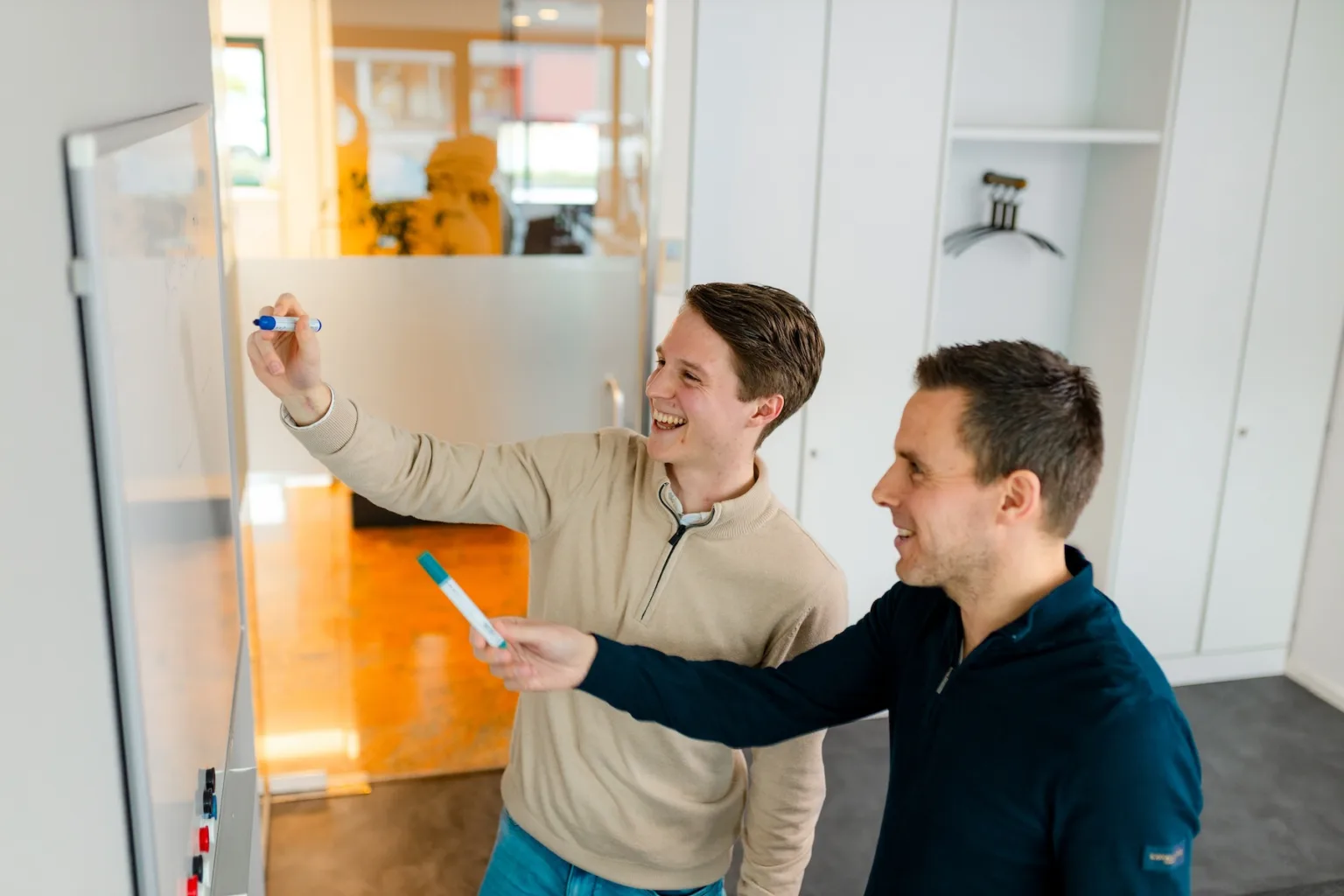 Twee collega’s van OneLane overleggen bij een whiteboard